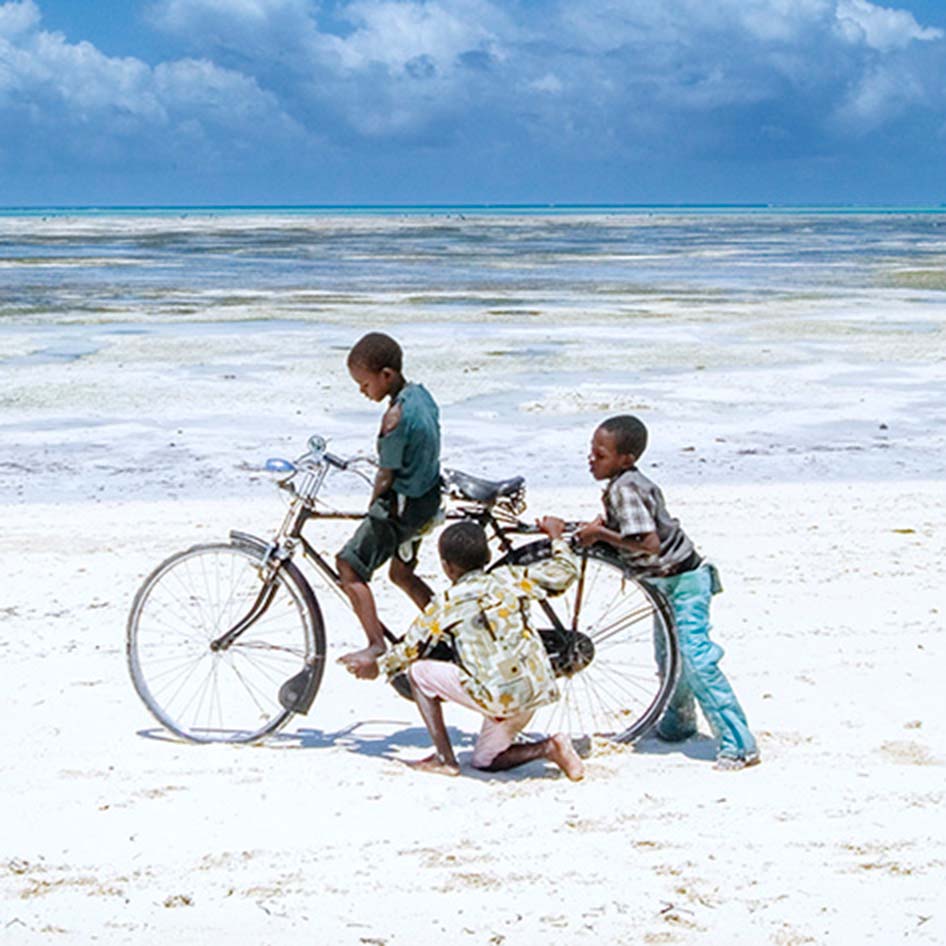 Three children playing with a bicycle on the beach