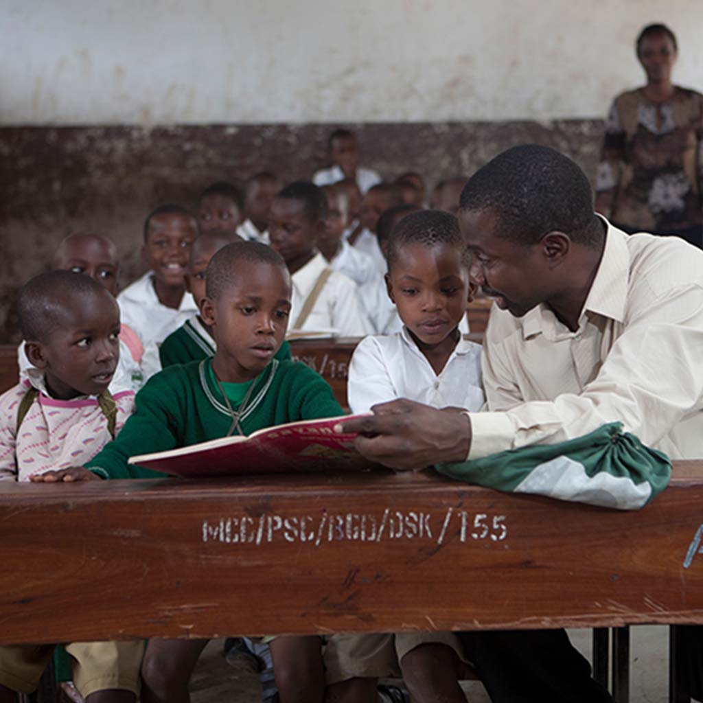 Teacher sitting and reading with students in classroom in Africa